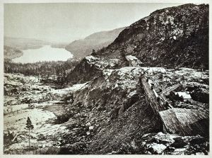 Lake beside snowy mountains with railroad construction sheds in foreground